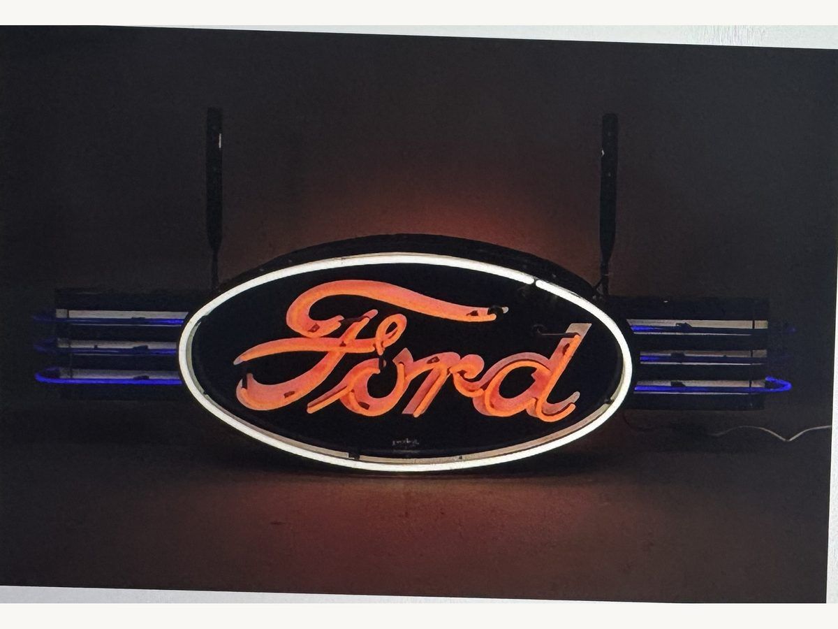 Lit Ford oval neon sign with red script lettering and blue neon wings